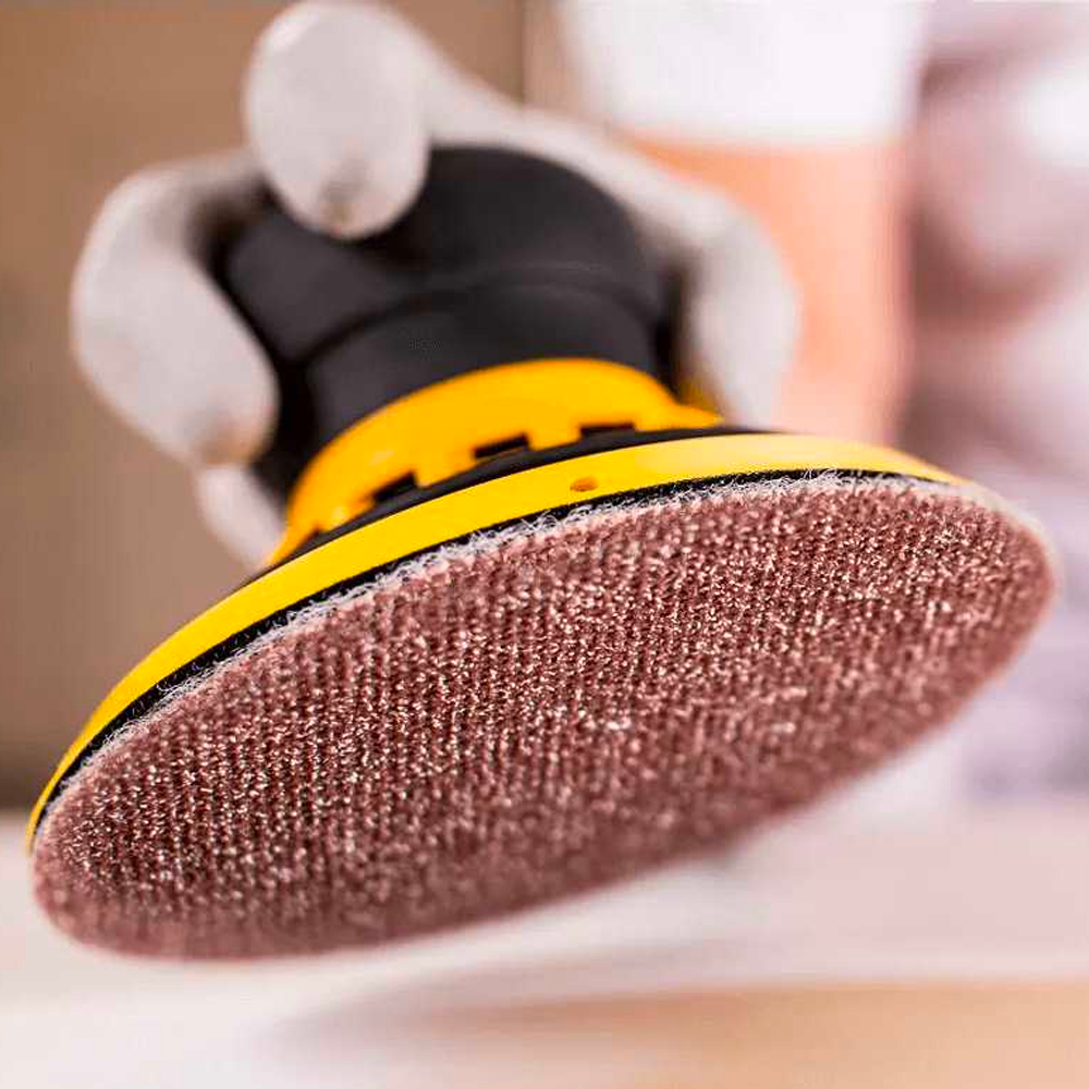 Hand holding a Mirka sander with a heavy-duty Abranet Ace HD disc attached to the grip pad