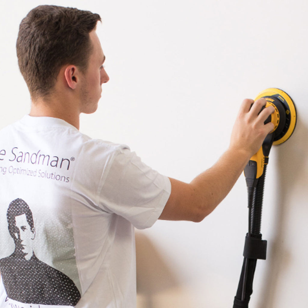 Tradie sanding a vertical wall with Mirka DEROS attached to a dust extractor vacuum
