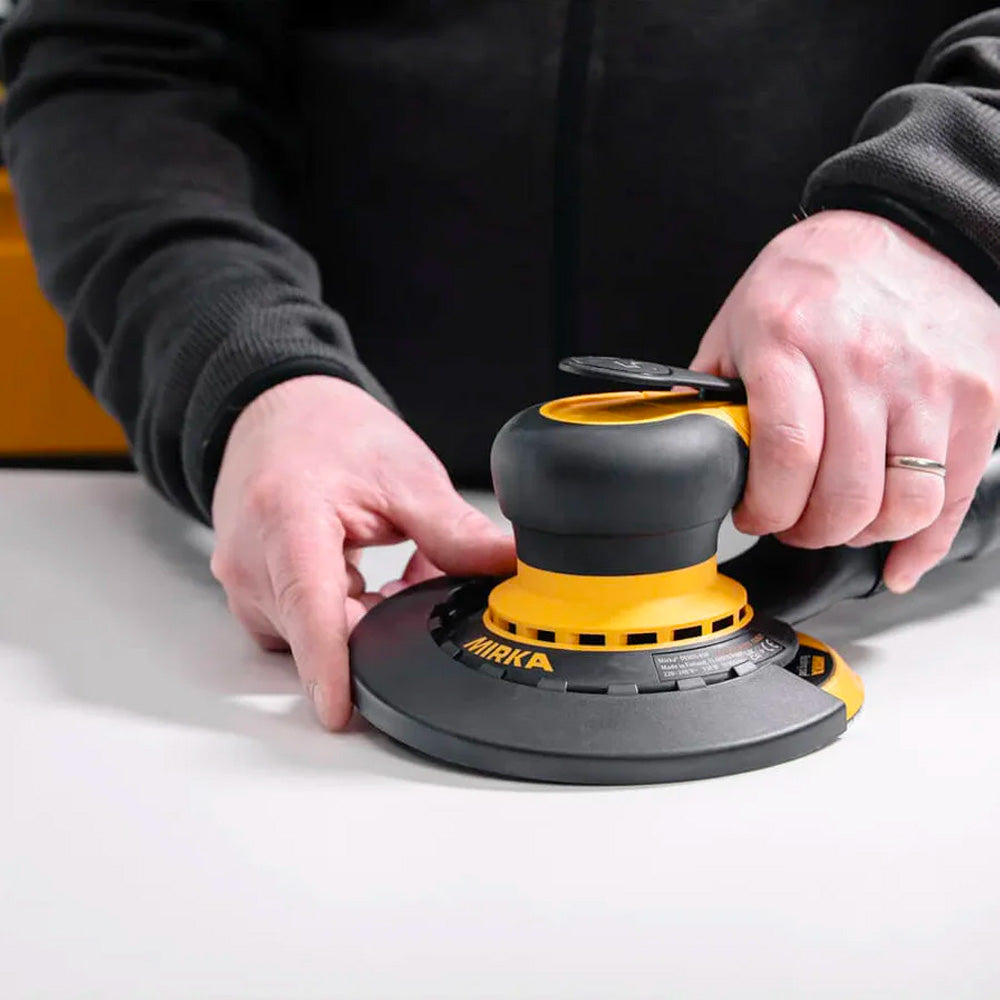 Hand fitting a black Mirka edge protector onto a DEROS orbital sander