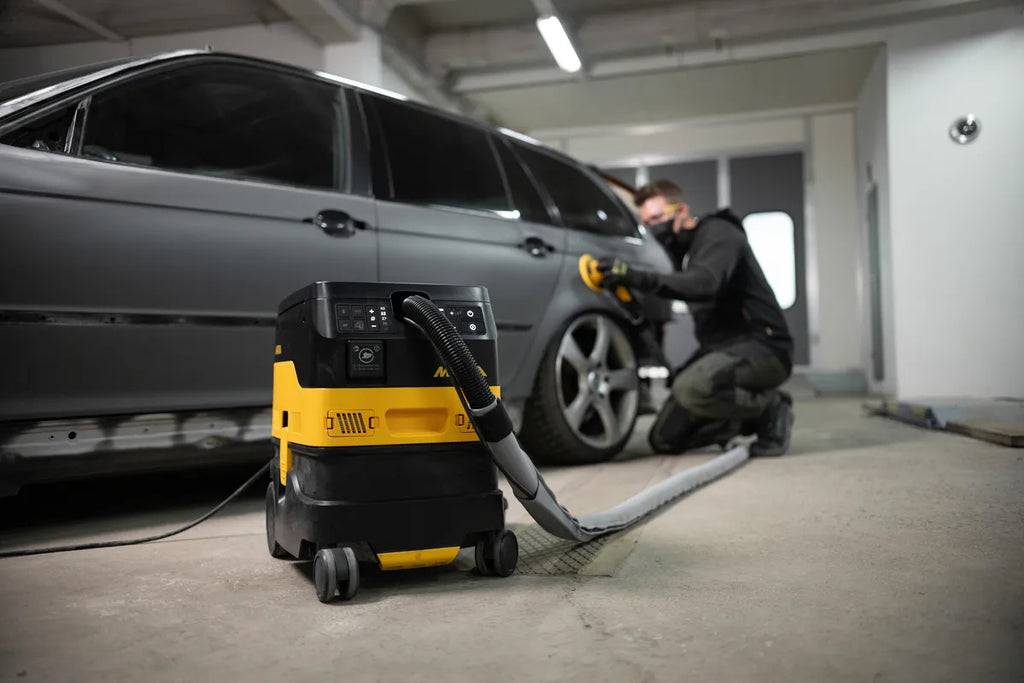 Professional using a sleeved Mirka hose for dust-free sanding in an automotive workshop