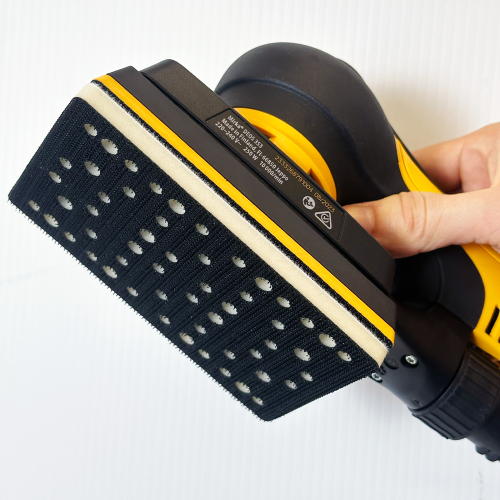 Hand holding a Mirka DEOS 353 sander with a 7mm thick interface pad fitted to the base