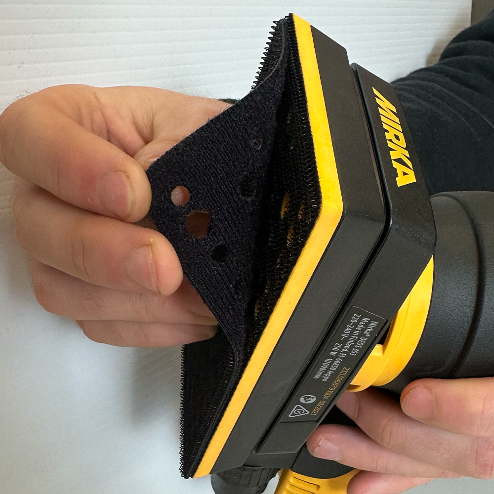 Tradie peeling back a 54-hole pad saver from a Mirka DEOS sander to show grip attachment